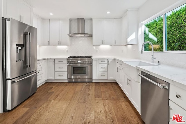 kitchen with white cabinets, light wood-type flooring, premium appliances, and wall chimney range hood