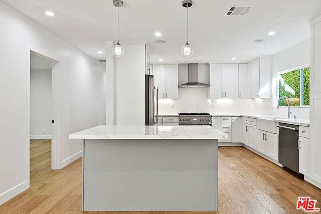 kitchen with a center island, wall chimney exhaust hood, light hardwood / wood-style floors, white cabinets, and appliances with stainless steel finishes