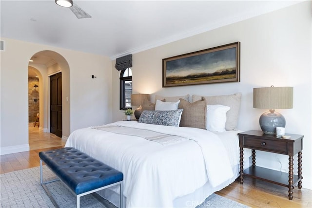 bedroom featuring light wood-style floors, baseboards, arched walkways, and crown molding