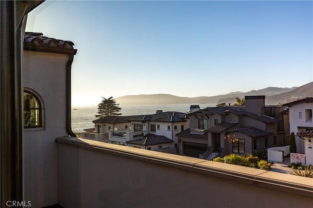 balcony at dusk featuring a water and mountain view