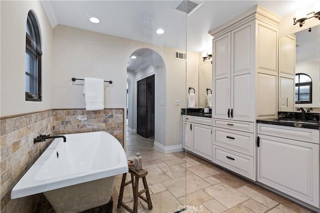 bathroom featuring a freestanding bath, vanity, visible vents, and stone tile floors