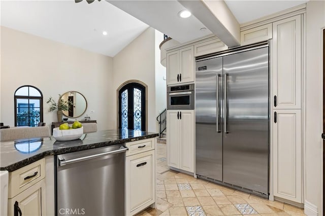 kitchen featuring cream cabinetry, plenty of natural light, dark stone counters, and appliances with stainless steel finishes