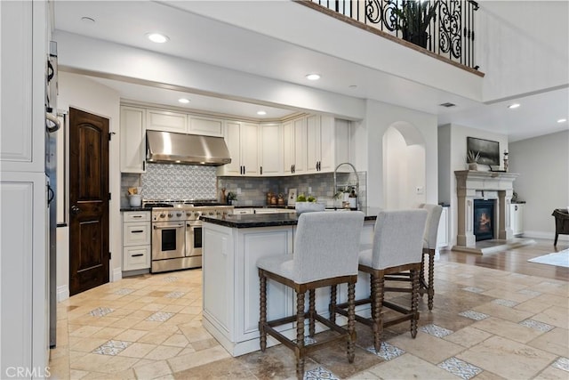 kitchen featuring double oven range, white cabinets, a kitchen breakfast bar, and kitchen peninsula