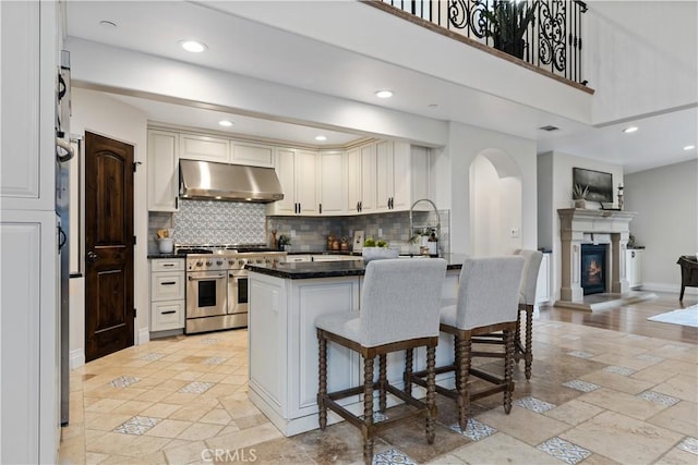 kitchen with range with two ovens, under cabinet range hood, a peninsula, open floor plan, and dark countertops