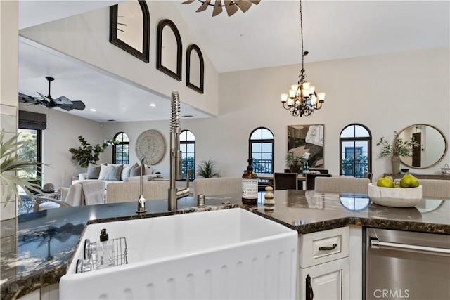 kitchen with sink, dark stone countertops, hanging light fixtures, white cabinets, and ceiling fan with notable chandelier