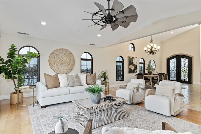 living room featuring french doors, ceiling fan with notable chandelier, light hardwood / wood-style floors, and vaulted ceiling