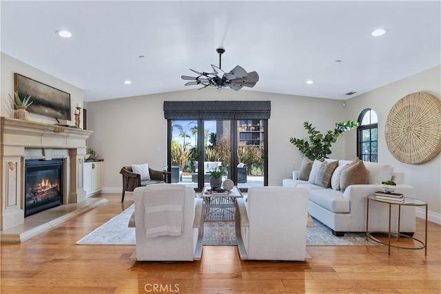 living area with baseboards, a glass covered fireplace, light wood-style flooring, vaulted ceiling, and recessed lighting