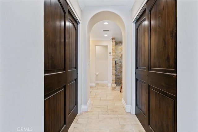 hallway with arched walkways, crown molding, stone tile flooring, visible vents, and baseboards