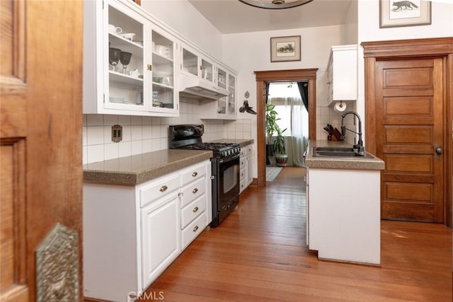 kitchen featuring white cabinetry, sink, black gas range oven, backsplash, and hardwood / wood-style floors