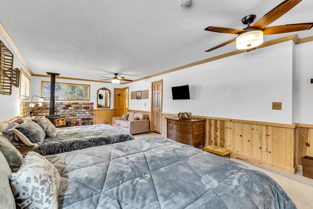 bedroom with light carpet, a wood stove, ceiling fan, and crown molding