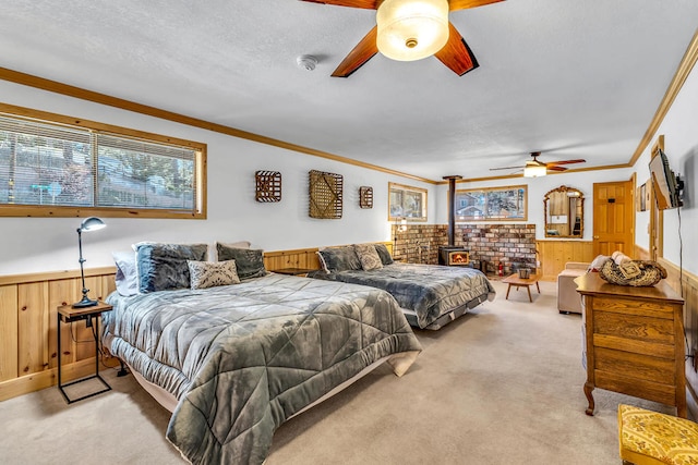 carpeted bedroom with wooden walls, a wood stove, ornamental molding, a textured ceiling, and ceiling fan