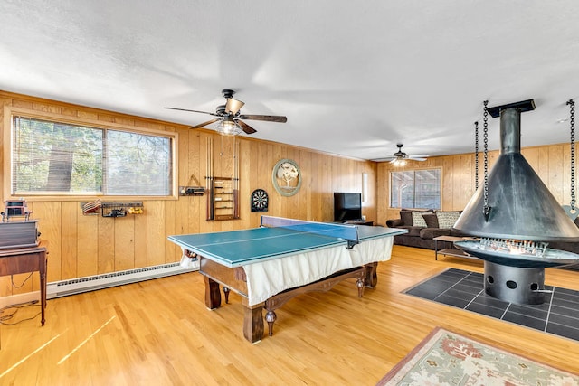 recreation room featuring baseboard heating, wood walls, wood-type flooring, and a wood stove