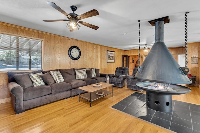 living room featuring light hardwood / wood-style floors, wood walls, a wood stove, and ceiling fan