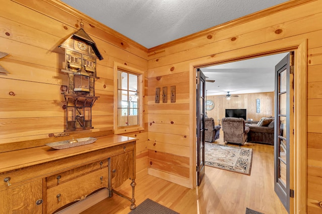 interior space featuring light hardwood / wood-style flooring, a textured ceiling, wooden walls, and ceiling fan