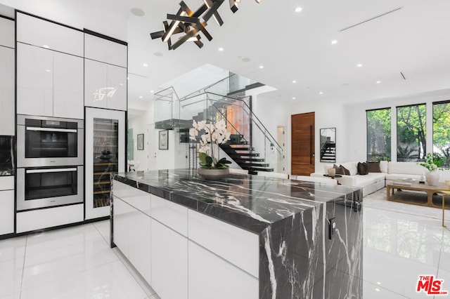 kitchen featuring light tile patterned floors, dark stone counters, stainless steel double oven, and white cabinets