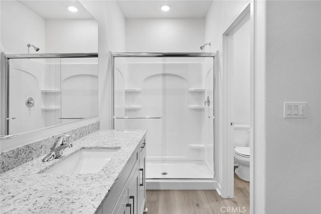 bathroom with vanity, a shower with shower door, hardwood / wood-style flooring, and toilet