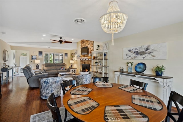 dining room with a stone fireplace, hardwood / wood-style floors, and ceiling fan with notable chandelier