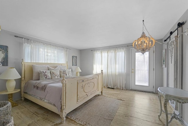 bedroom featuring access to outside, light hardwood / wood-style flooring, a barn door, and a notable chandelier