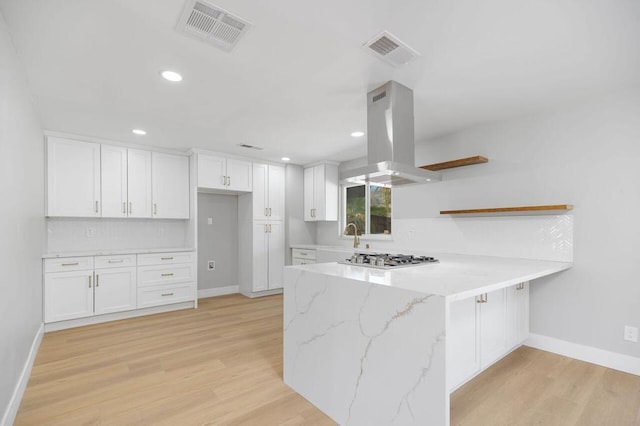 kitchen featuring white cabinetry, light stone countertops, stainless steel gas stovetop, island range hood, and light hardwood / wood-style floors