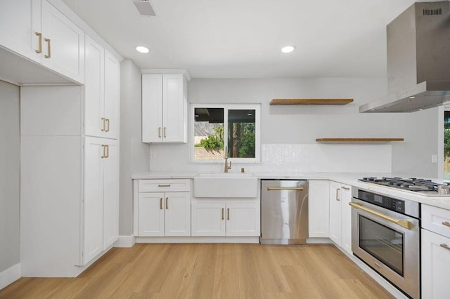 kitchen with wall chimney range hood, white cabinets, light hardwood / wood-style flooring, sink, and stainless steel appliances