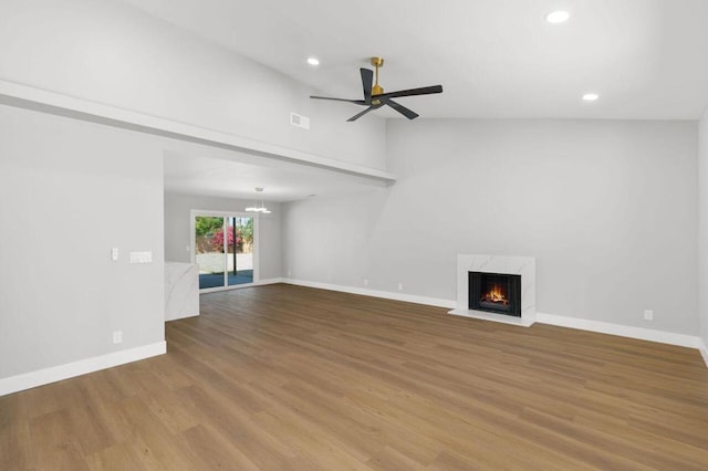 unfurnished living room with ceiling fan, vaulted ceiling, a high end fireplace, and hardwood / wood-style floors