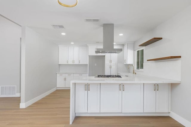 kitchen with kitchen peninsula, stainless steel gas stovetop, white cabinetry, island range hood, and light wood-type flooring