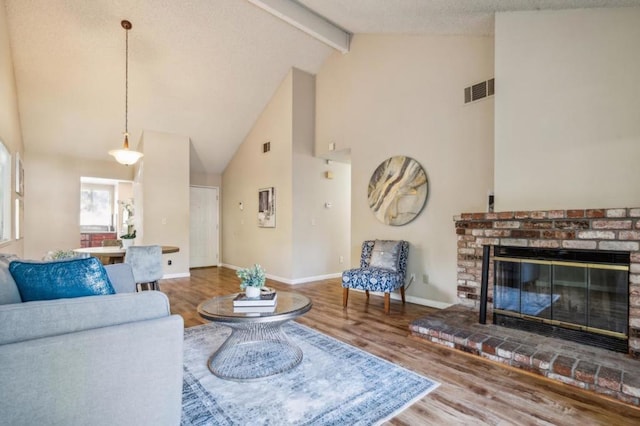 living room with high vaulted ceiling, a fireplace, hardwood / wood-style flooring, beam ceiling, and a textured ceiling