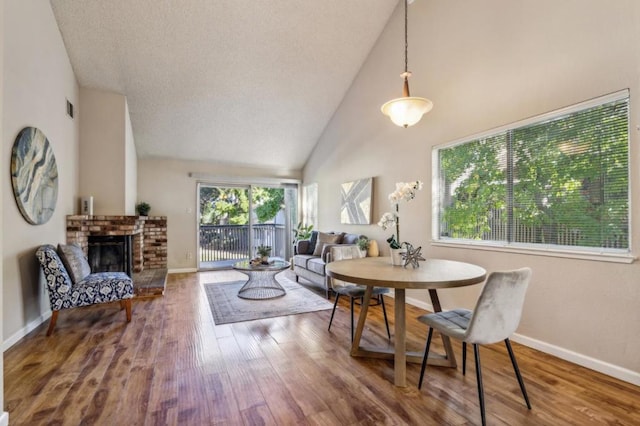 dining space featuring wood-type flooring, a fireplace, and high vaulted ceiling