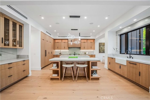 kitchen featuring a kitchen breakfast bar, sink, decorative light fixtures, a center island, and light hardwood / wood-style floors