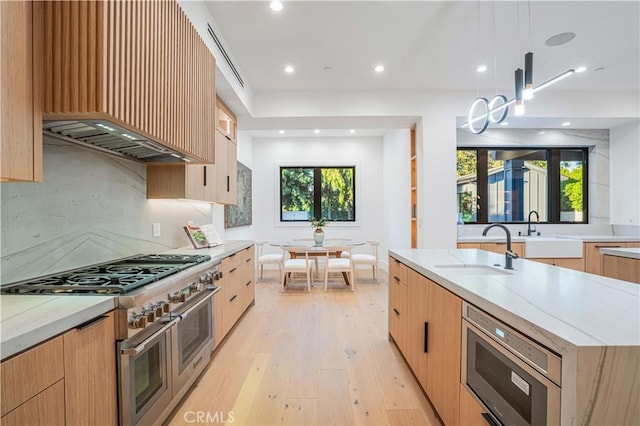 kitchen featuring light stone countertops, appliances with stainless steel finishes, sink, light hardwood / wood-style floors, and hanging light fixtures