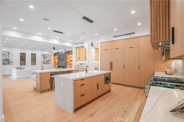 kitchen with a large island, sink, decorative light fixtures, light hardwood / wood-style flooring, and a breakfast bar area