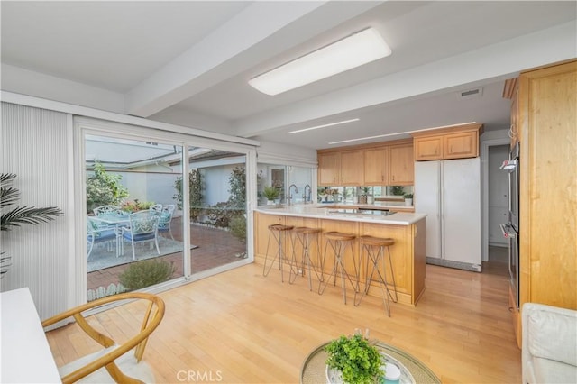 kitchen featuring a breakfast bar area, light wood-type flooring, kitchen peninsula, white fridge, and beamed ceiling