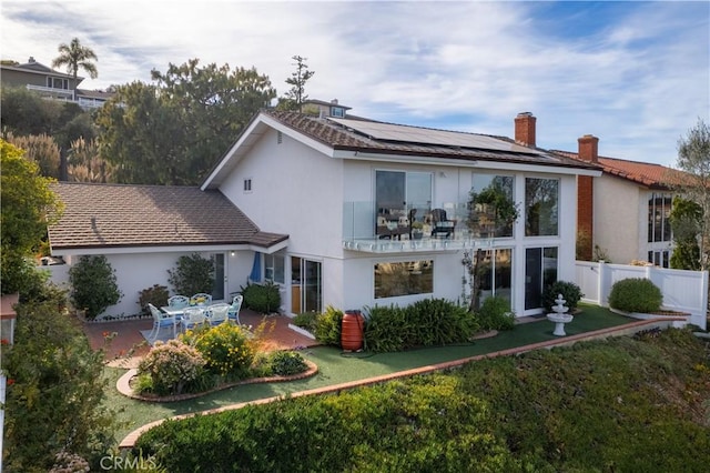 back of house with solar panels, a patio, and a lawn