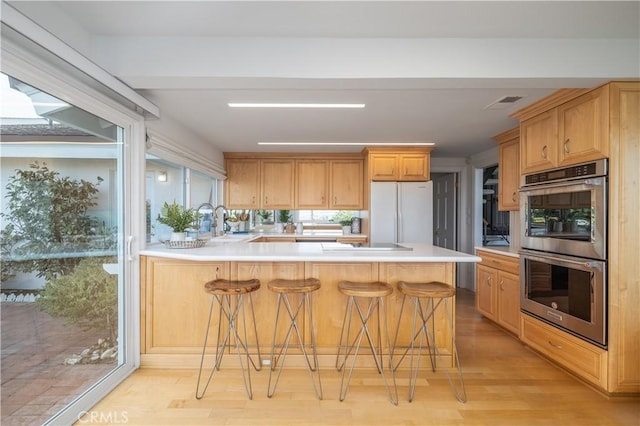 kitchen with a kitchen breakfast bar, white refrigerator, kitchen peninsula, stainless steel double oven, and light hardwood / wood-style flooring