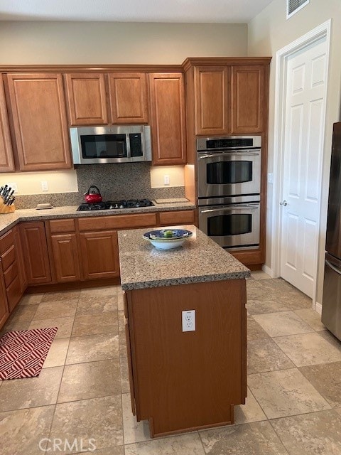 kitchen featuring a center island, stainless steel appliances, dark stone counters, and backsplash