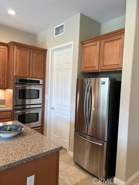 kitchen with stainless steel appliances, dark stone counters, and light tile patterned floors