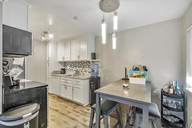 kitchen featuring backsplash, light hardwood / wood-style flooring, dishwasher, white cabinets, and hanging light fixtures