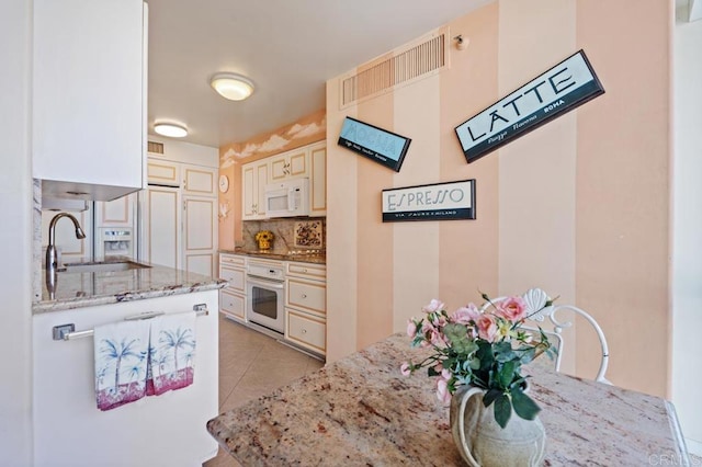 kitchen with decorative backsplash, light tile patterned floors, sink, light stone counters, and white appliances