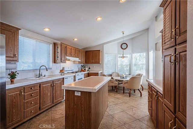 kitchen featuring white gas range, sink, hanging light fixtures, vaulted ceiling, and a kitchen island