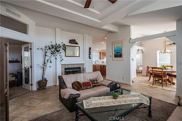 living room featuring ceiling fan with notable chandelier, light tile patterned floors, sink, and a tiled fireplace