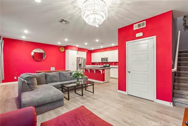 living room featuring sink, light hardwood / wood-style flooring, and an inviting chandelier