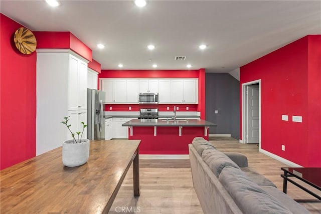 kitchen with appliances with stainless steel finishes, light wood-type flooring, a kitchen island with sink, sink, and white cabinetry