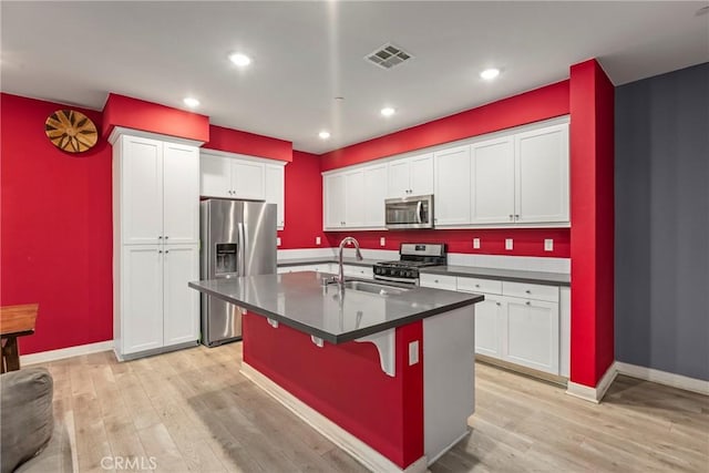 kitchen with sink, stainless steel appliances, an island with sink, a breakfast bar, and light wood-type flooring