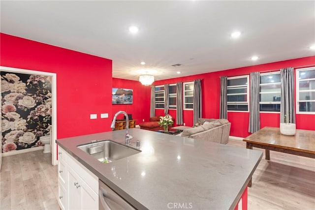 kitchen with light wood-type flooring, a kitchen island with sink, sink, dishwasher, and white cabinets