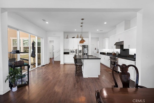 kitchen with white cabinetry, stainless steel appliances, decorative light fixtures, a kitchen island with sink, and a breakfast bar