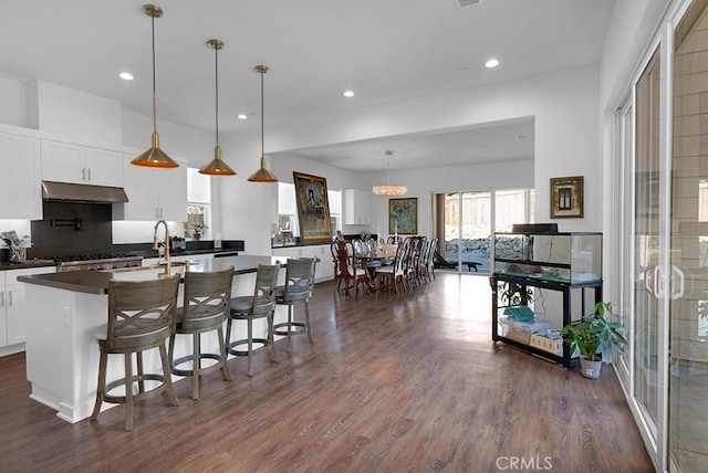 kitchen with white cabinetry, dark wood-type flooring, hanging light fixtures, a kitchen breakfast bar, and tasteful backsplash