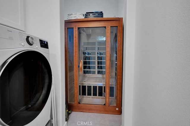 laundry area with stacked washer / drying machine and light tile patterned floors