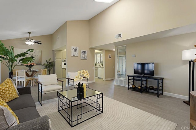 living room featuring light hardwood / wood-style flooring, high vaulted ceiling, and ceiling fan