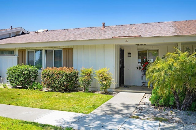 doorway to property featuring board and batten siding, a lawn, and a shingled roof