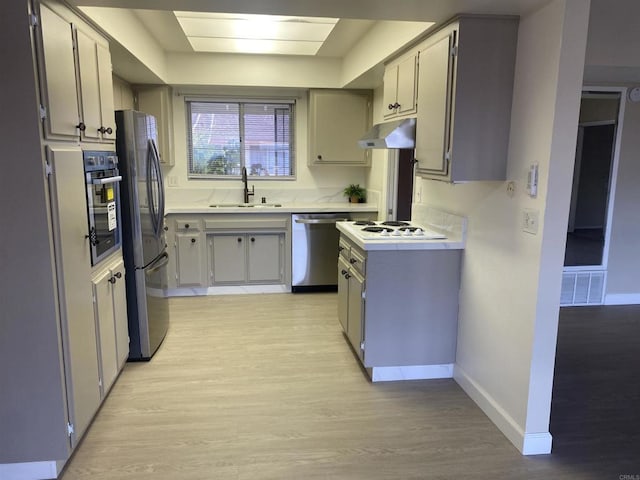 kitchen featuring light wood finished floors, stainless steel appliances, light countertops, a sink, and under cabinet range hood